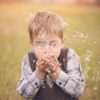boy blowing hands filled with dandelion flowers
