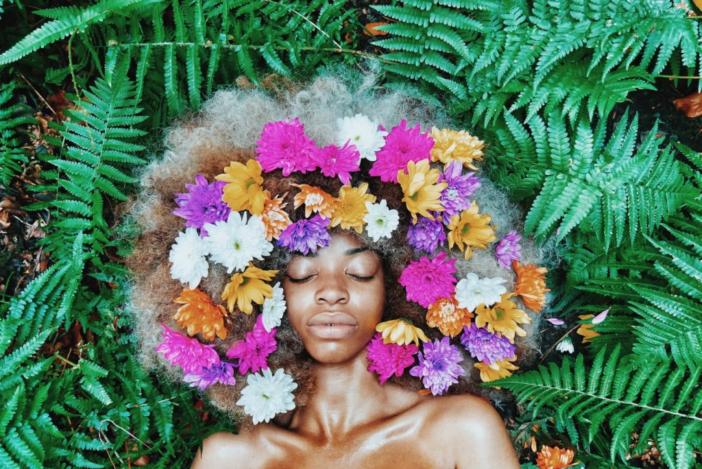 woman with floral headdress lying on green leaf plants
