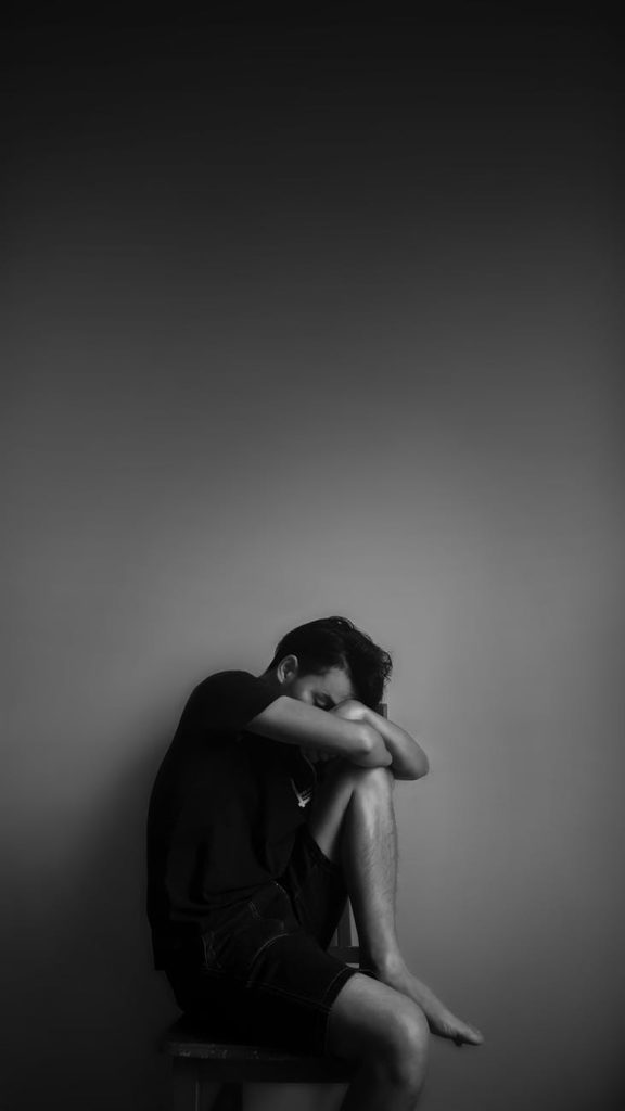 grayscale photography of man sitting beside wall