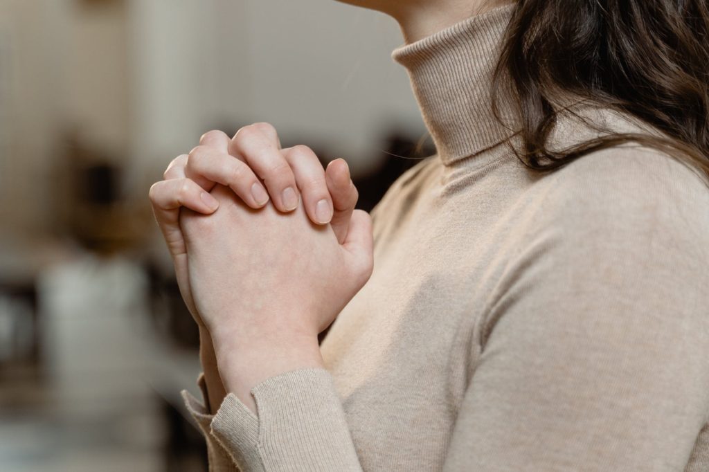 woman in brown turtle neck shirt with hands clasped
