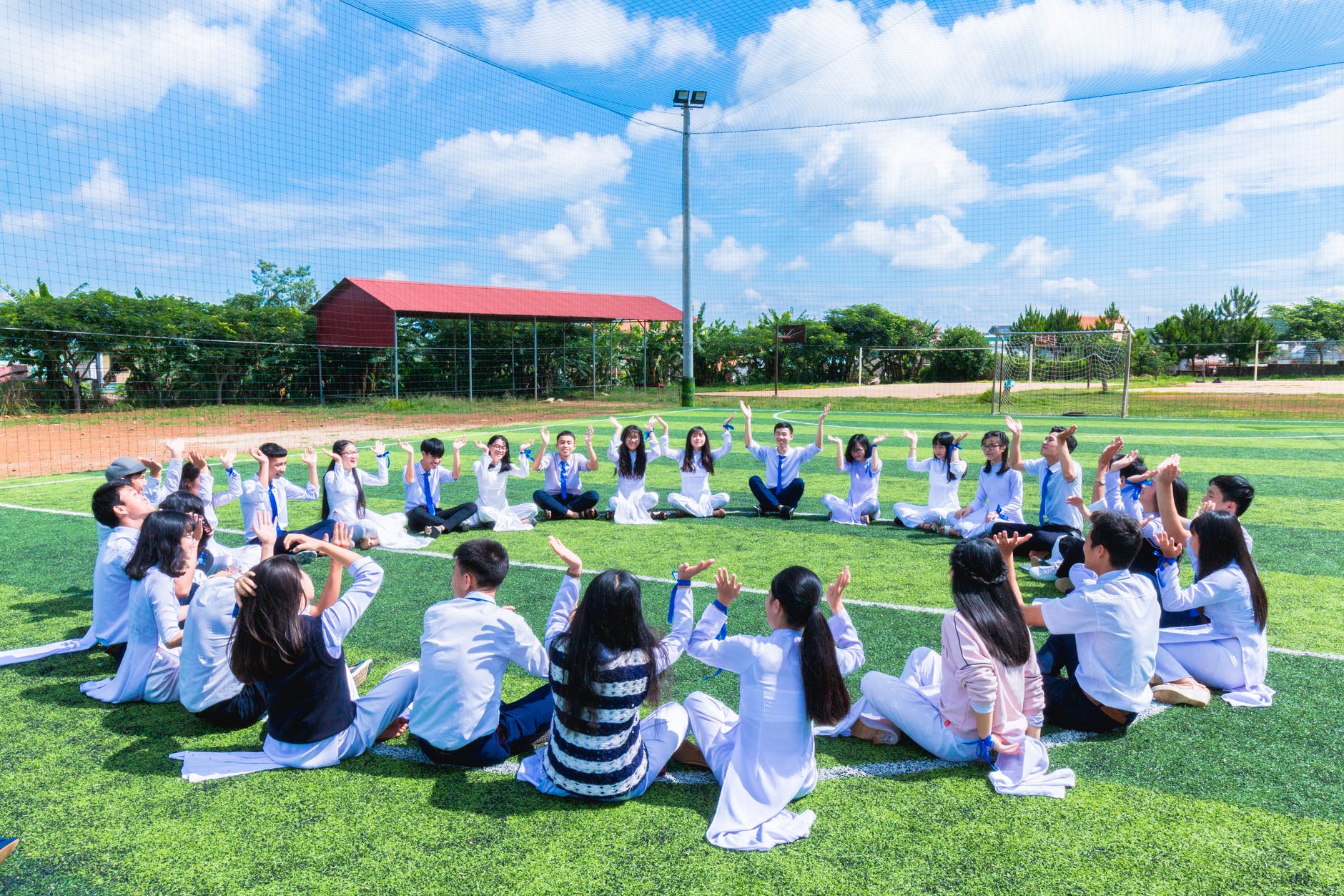 people sitting on green lawn grass while doing hands up at daytime