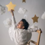 happy black boy reaching out to decorative star from chair