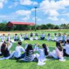 people sitting on green lawn grass while doing hands up at daytime