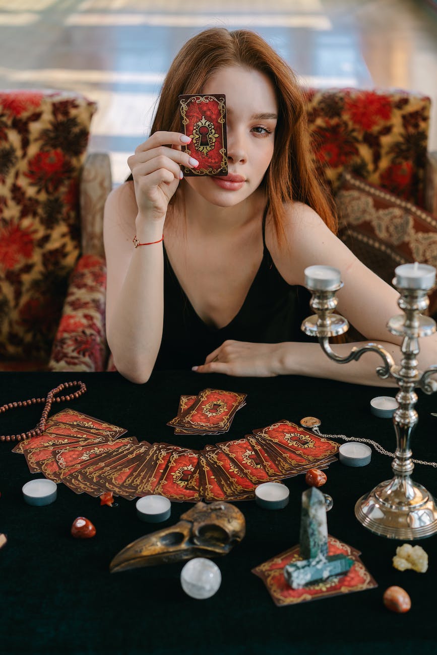 a woman in black tank top holding a tarot card while covering her one eye