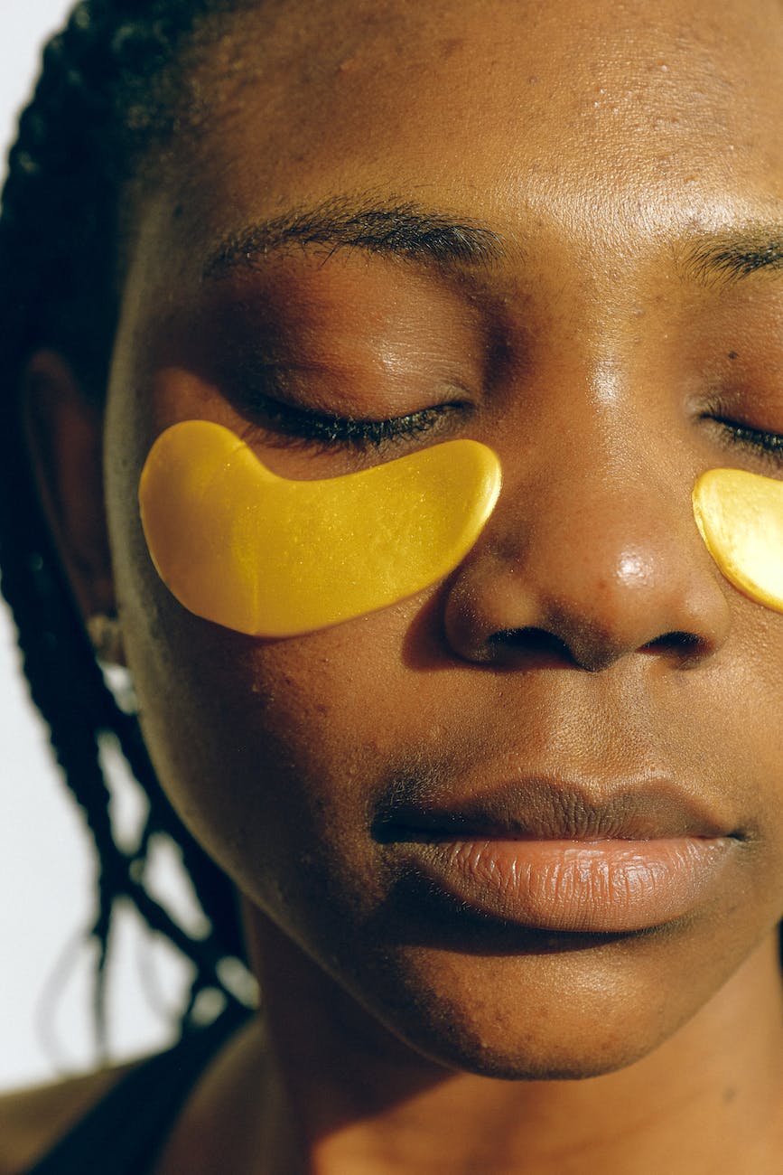 young peaceful black woman applying golden collagen eye patches