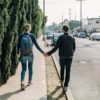 man holding woman while walking on sidewalk