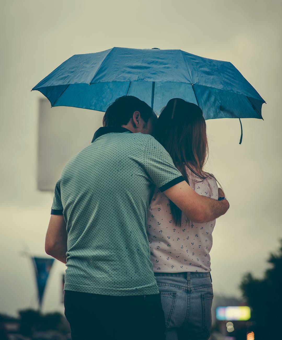 man hugging woman while holding umbrella