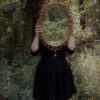 woman holding mirror against her head in the middle of forest