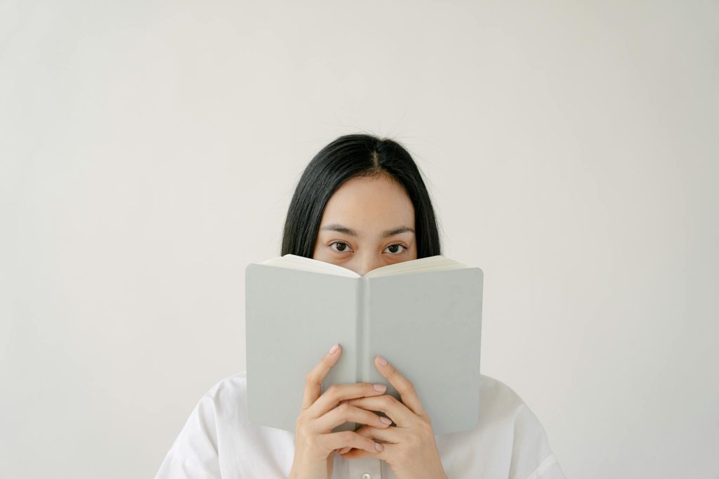 young asian lady covering mouth with copybook